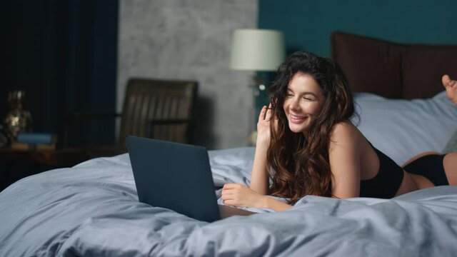 Girl greeting interlocutor laptop screen bed. Sexy woman relaxing with computer.