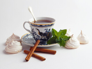 A mug of tea surrounded by meringue cakes. On a white background, cinnamon and mint.