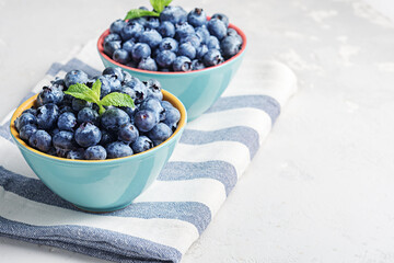 Fresh blueberries in bowls on a concrete surface with a copy of space.