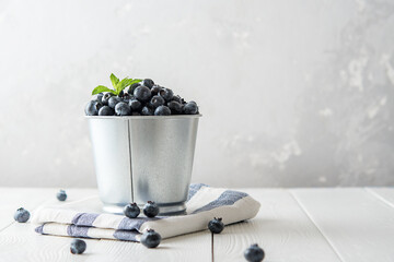 Fresh blueberries in a metal pot on a light wooden table with a copy of space.