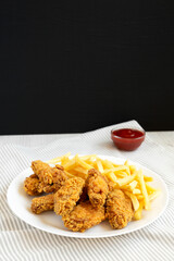 Homemade Crispy Chicken Wings and French Fries on a white plate, side view. Copy space.