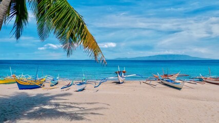 Traditional Filipino outrigger boats on a beautiful white sand beach, with turquoise water and blue sky in the resort area of Puerto Galera on the tropical island of Mindoro in the Philippines.