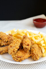 Homemade Crispy Chicken Wings and French Fries on a white plate, side view.