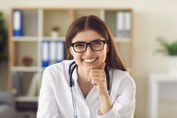 Portrait of friendly young female physician at desk in office smiling to patient