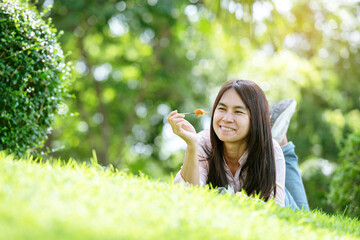 Relax beautiful asian woman smiling face Lying down on green grass field in outdoors garden park enjoy nature morning. Freedom Lifestyle woman breathing fresh air in green park on spring lawn outdoors