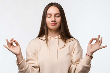 Young pretty woman with long chestnut hair straight hair keeps hands in mudra gesture, holds...