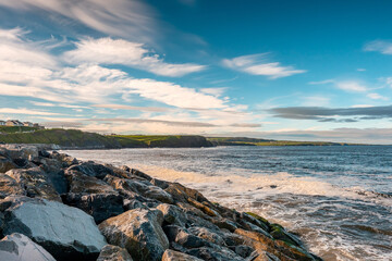 Rocks on a shore and Atlantic ocean, Lahinch town, county Clare, Ireland, Warm sunny day with cloudy sky. Nobody.