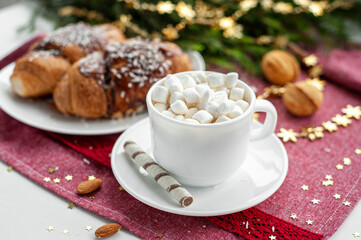 Christmas breakfast. Christmas morning. A cup of coffee or cocoa with marshmallows and sweets. On a red tablecloth next to a branch decorated with Christmas spruce. Selective focus.
