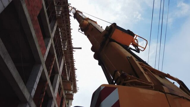 Yellow automobile crane with risen telescopic boom outdoors over blue sky, construction site