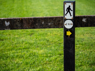 Sign on a fence walking man and direction arrow to the right. and 2 km distance. Green grass in the background.  Concept trekking and hiking routes and outdoor activity.