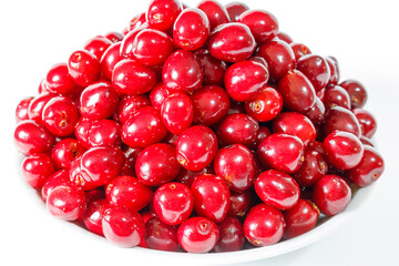 Red cherries lie on a white plate on a white background