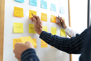 Team working in office putting sticky note on white board analyzing strategy of business.