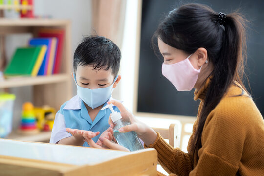 Asian Woman Teacher Use Alcohol Gel On Hand Of Her Student For Prevent Virus From Covid19 In Classroom In Preschool.