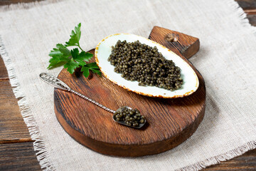 Black caviar. Black sturgeon caviar in a ceramic bowl and in a metal spoon on a wooden serving Board. A healthy treat. Space for text	