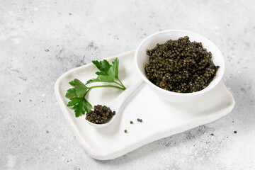 Black caviar. Black sturgeon caviar in a ceramic bowl and in a ceramic spoon on a light background. Useful delicacy	