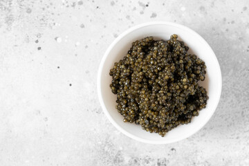 Black caviar. Black sturgeon caviar in a ceramic bowl and in a ceramic spoon on a light background. Useful delicacy. Top view with space for text	