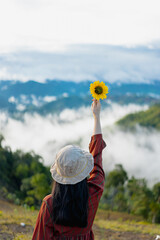 Photo from the back of a woman in red dress holding an artificial sunflower with her right hand up...