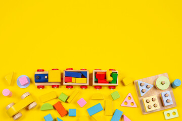 Baby kids toys background. Wooden train, educational stacking color recognition puzzle toy and colorful blocks on yellow background. Top view