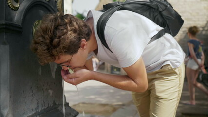 Fototapeta na wymiar Closeup young guy drinking water at city fountain. Thirsty man drinking liquid