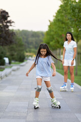 pretty mother and her little daughter rollerskating in summer park. happy family