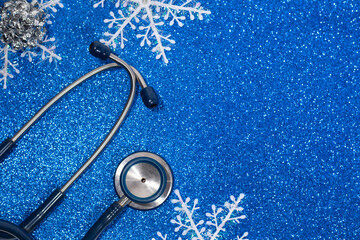Blue Stethoscope and white snowflakes close-up on the left on a blue holiday background with glitter.The view from the top.