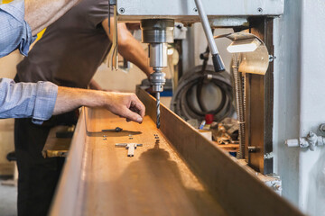 factory worker makes holes in a metal beam using a drilling machine