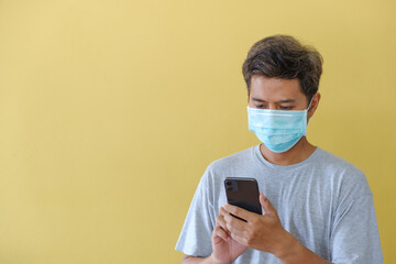 the man wearing masks and using mobile phone for safety in the face of the COVID epidemic stand in front of a yellow scene.
