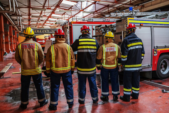 Rear view of group of firefighters in protective uniforms and helmets prepared for action.