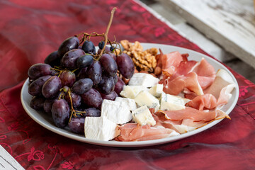 Talerz z prosciutto, serem brie i gorgonzolą, orzechami greckimi i winogronem.