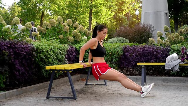 young brunette sports woman makes bench dip at the park at warm summer day