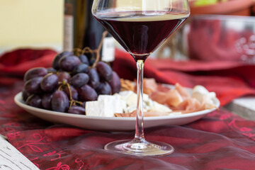 Wino czerwone i kieliszek .Talerz z prosciutto, serem brie i gorgonzolą, orzechami greckimi i winogronem. - obrazy, fototapety, plakaty