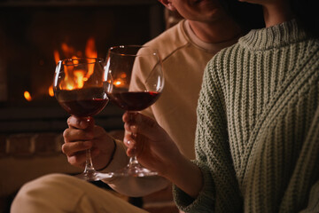 Couple with glasses of red wine near fireplace, closeup