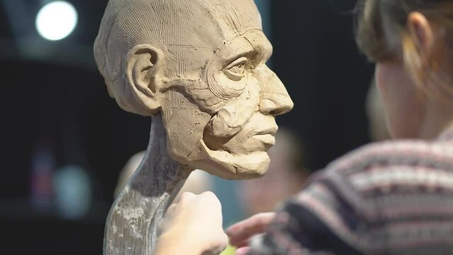 Woman sculptor at work on a sculpture of a human head. The process of restoring the shape of the cheek bone. Side view. Close up view.