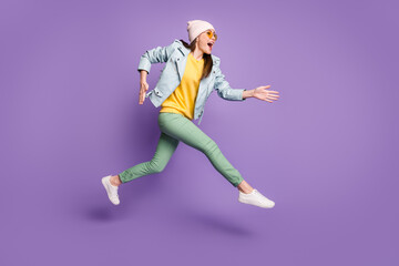 Fototapeta na wymiar Full body profile side photo of surprised shocked cheerful girl jump run after discounts wear yellow green headwear pants isolated over violet color background
