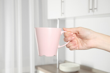 Woman holding pink cup at home, closeup