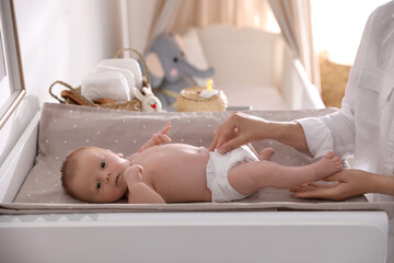 Mother changing her baby's diaper on table in room
