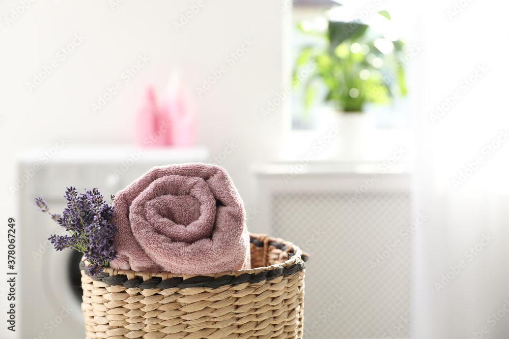 Wall mural Wicker basket with rolled clean towel and lavender flowers indoors. Space for text