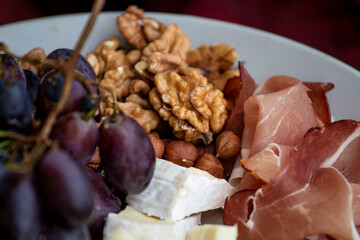 Talerz z prosciutto, serem brie i gorgonzolą, orzechami greckimi i winogronem.