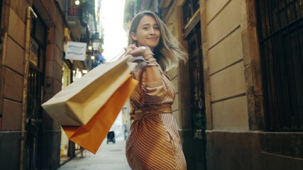 Back view of woman walking with shopping bags. Smiling girl flirting on camera