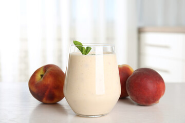 Tasty milk shake and fresh peaches on white table