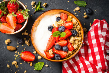 Greek yogurt granola with fresh berries on black stone table.