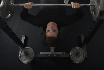 Top view of a young fit male doing a barbell bench press at the gym