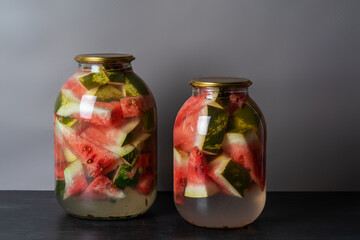 Pickled watermelon with herbs in a glass jar on a wooden table