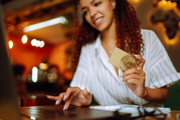Сredit card in female hand. African American woman sitting at cafe making online shopping. Online shopping, e-commerce, internet banking, spending money.