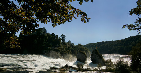 The Rhine Falls cascades with their thundering masses of water and the castle Laufen in the background.