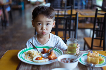 A cute Asian boy eating food and enjoying for breakfast by himself in the restaurant.
