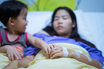 Woman patients lying on bed in hospital. Hands with saline solution. Her hand is held by her son's hand for encouragement.