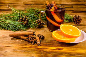 Cup of mulled wine with cinnamon, sliced orange and fir tree branches on wooden table