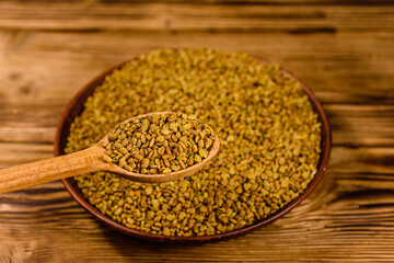 Ceramic plate and spoon with fenugreek seeds on wooden table