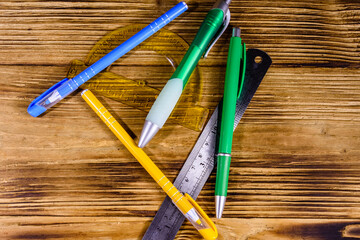 Multi colored ball pens, protractor and ruler on a wooden table. Top view